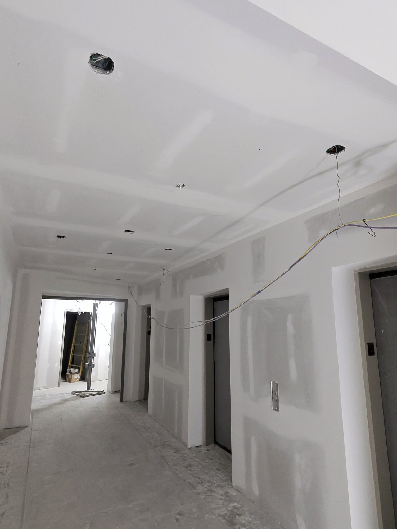 Long hallway, taped and sanded, warm light at the far end