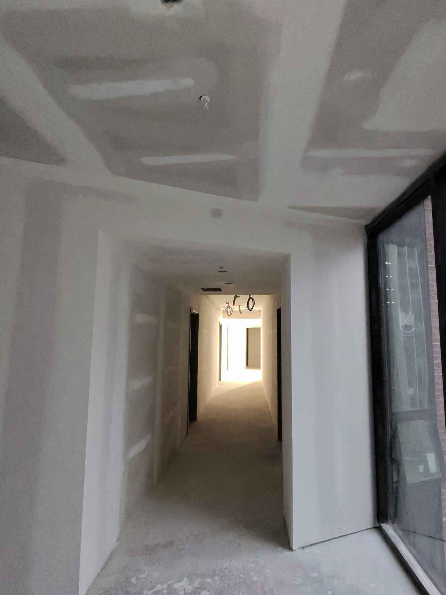Taped and sanded hallway, downtown high-rise, warm light at the end
